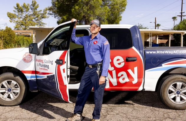 Técnico sorridente em uniforme azul ao lado de caminhonete de trabalho.