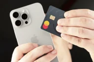 Mãos segurando um iPhone prateado e um cartão Mastercard de design escuro e minimalista.
