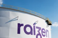 Tanque industrial branco com logotipo "raizen" em roxo, escada lateral e céu azul claro ao fundo. Investida da Cosan