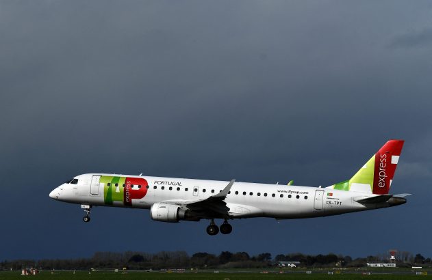 Avião da TAP Express, Embraer 190, aterrissando com trem de pouso estendido sob um céu escuro e nublado.