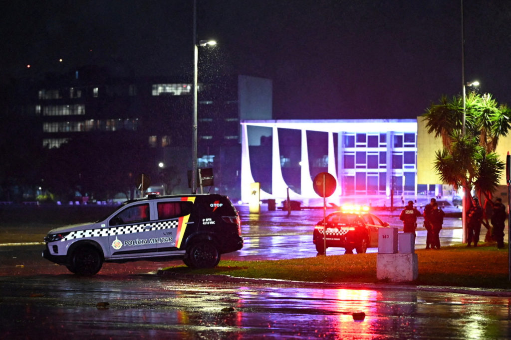Viaturas e policiais da PM à noite, em frente ao Palácio do Planalto, Brasília. Chão molhado reflete luzes.