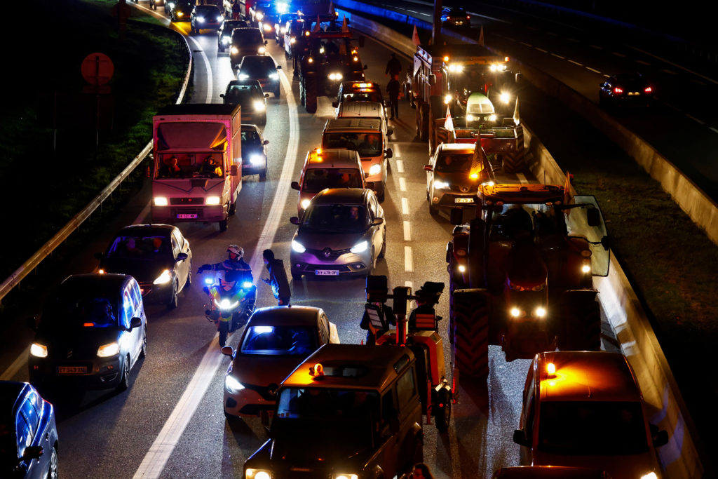 Bloqueio noturno em rodovia com tratores, carros, caminhões e luzes de emergência. Pessoas na pista.