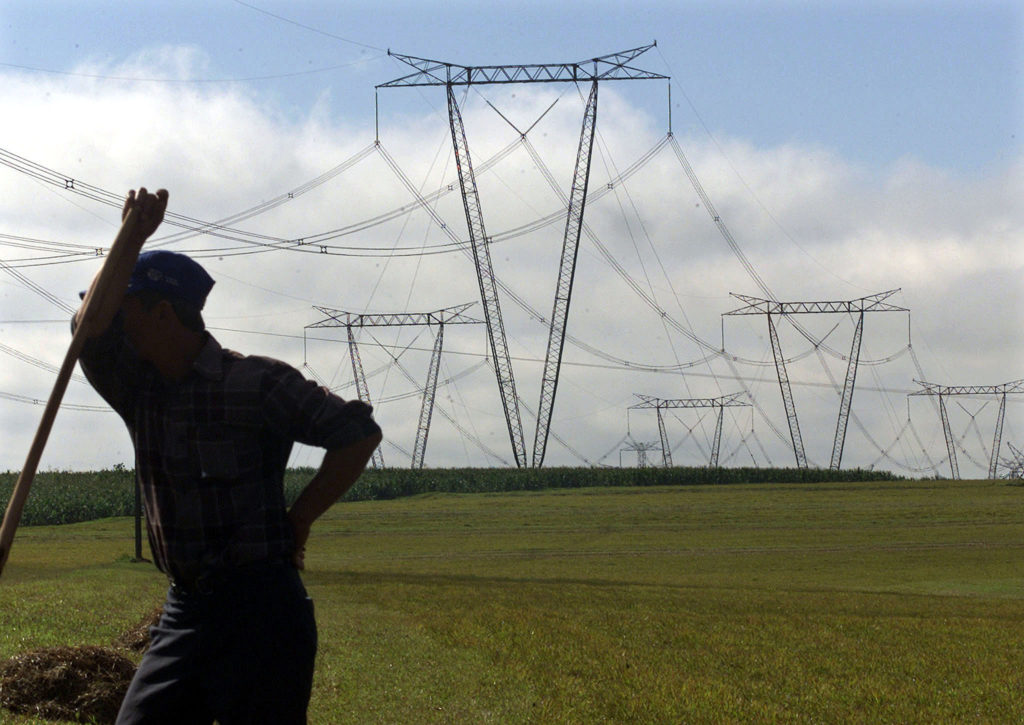 Pessoa de costas em campo verde, olhando para torres de transmissão de energia.