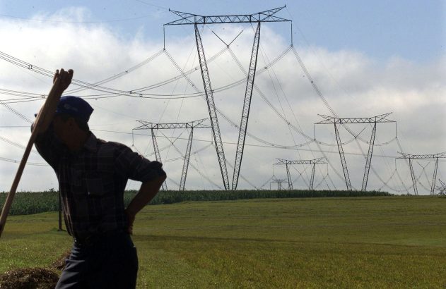 Pessoa de costas em campo verde, olhando para torres de transmissão de energia.