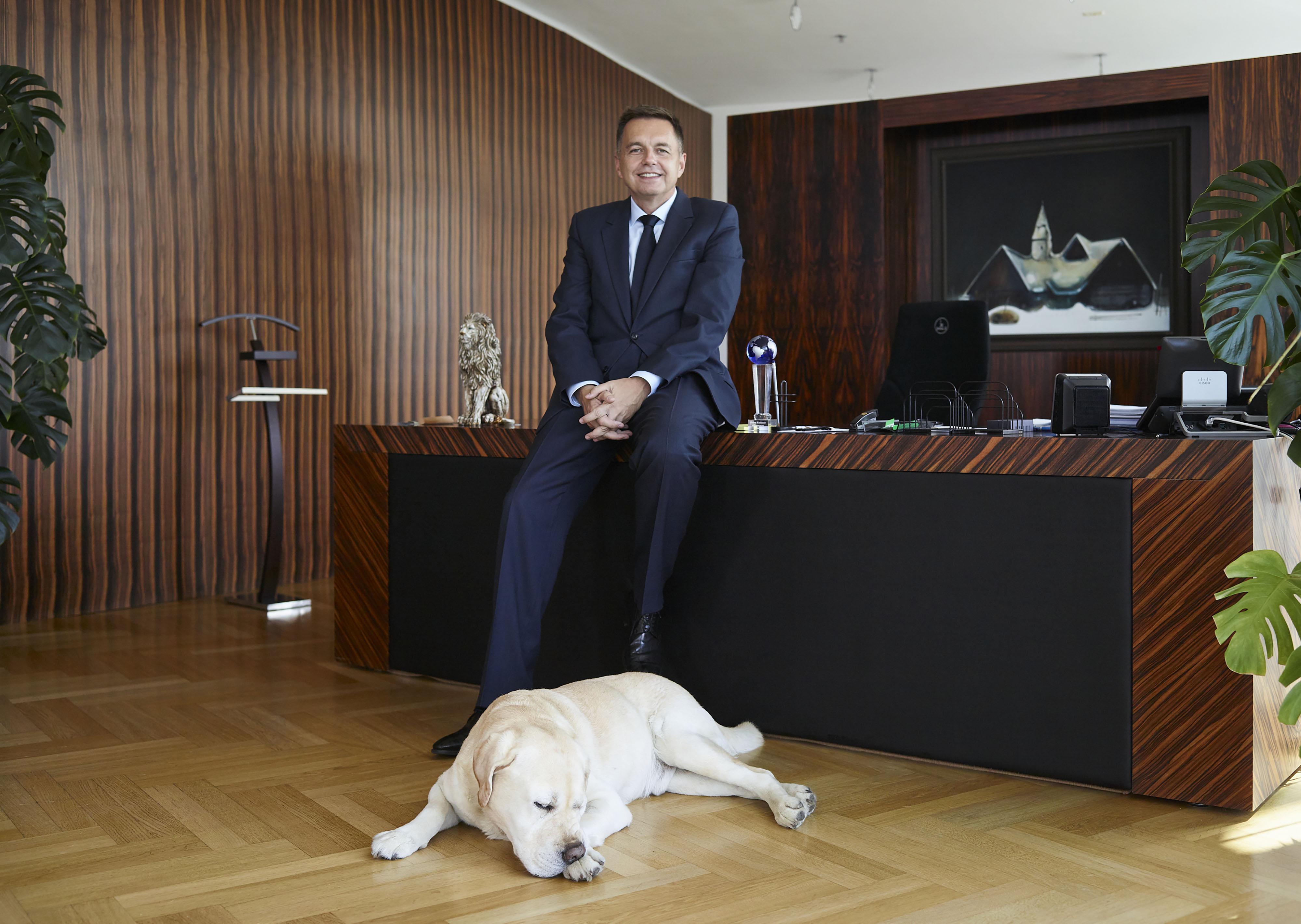 Homem de terno sentado em mesa de escritório, com labrador amarelo dormindo no chão.