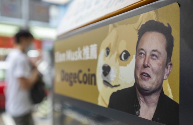 Letreiro mostra Elon Musk, meme Doge e "DogeCoin". Pessoa desfocada ao fundo.