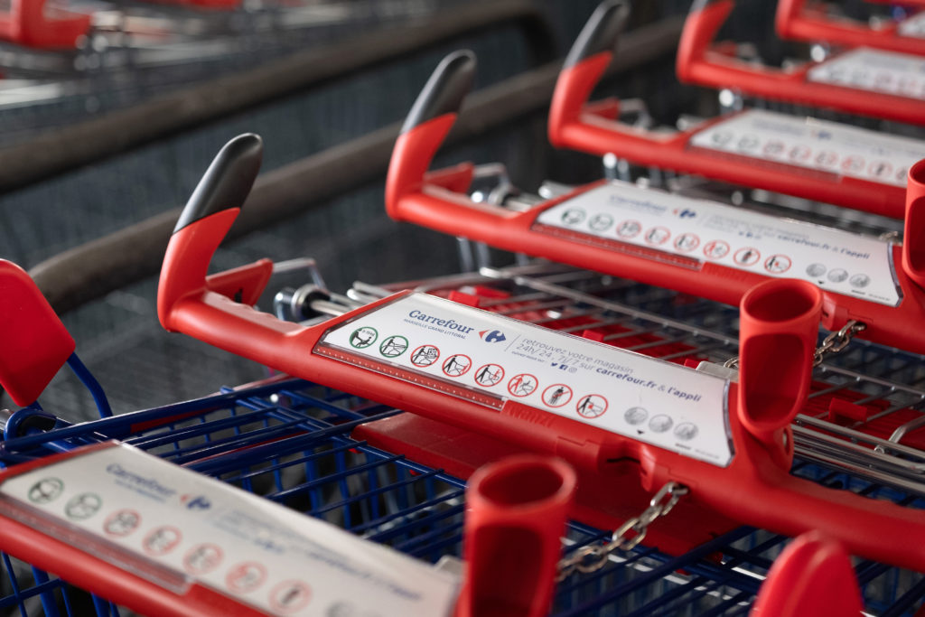 Carrinhos de supermercado vermelhos enfileirados, com placas brancas nas alças e correntes metálicas.