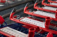 Carrinhos de supermercado vermelhos enfileirados, com placas brancas nas alças e correntes metálicas.