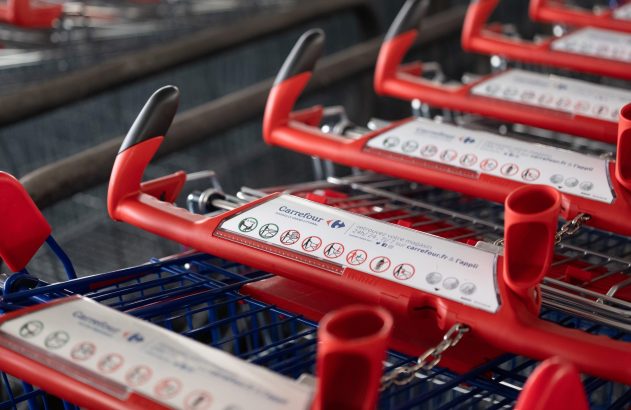 Carrinhos de supermercado vermelhos enfileirados, com placas brancas nas alças e correntes metálicas.