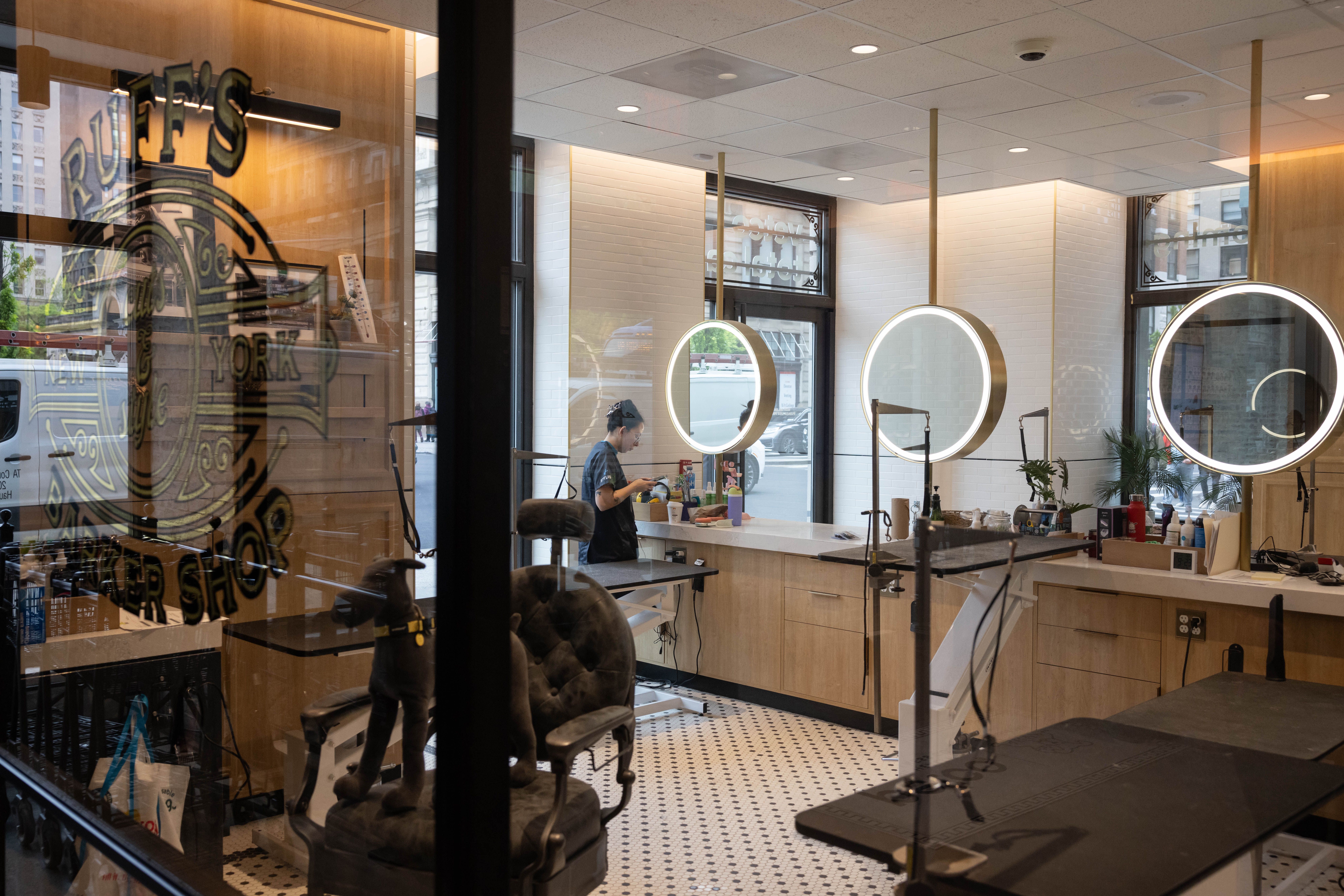 Interior de barbearia/salão moderno, com espelhos iluminados e profissional trabalhando.