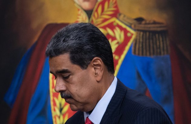 Nicolás Maduro de terno escuro e gravata vermelha caminha, com pintura de Simón Bolívar ao fundo.
