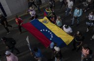 Multidão segura grande bandeira da Venezuela horizontalmente em rua escura. Cores e estrelas da bandeira são visíveis.
