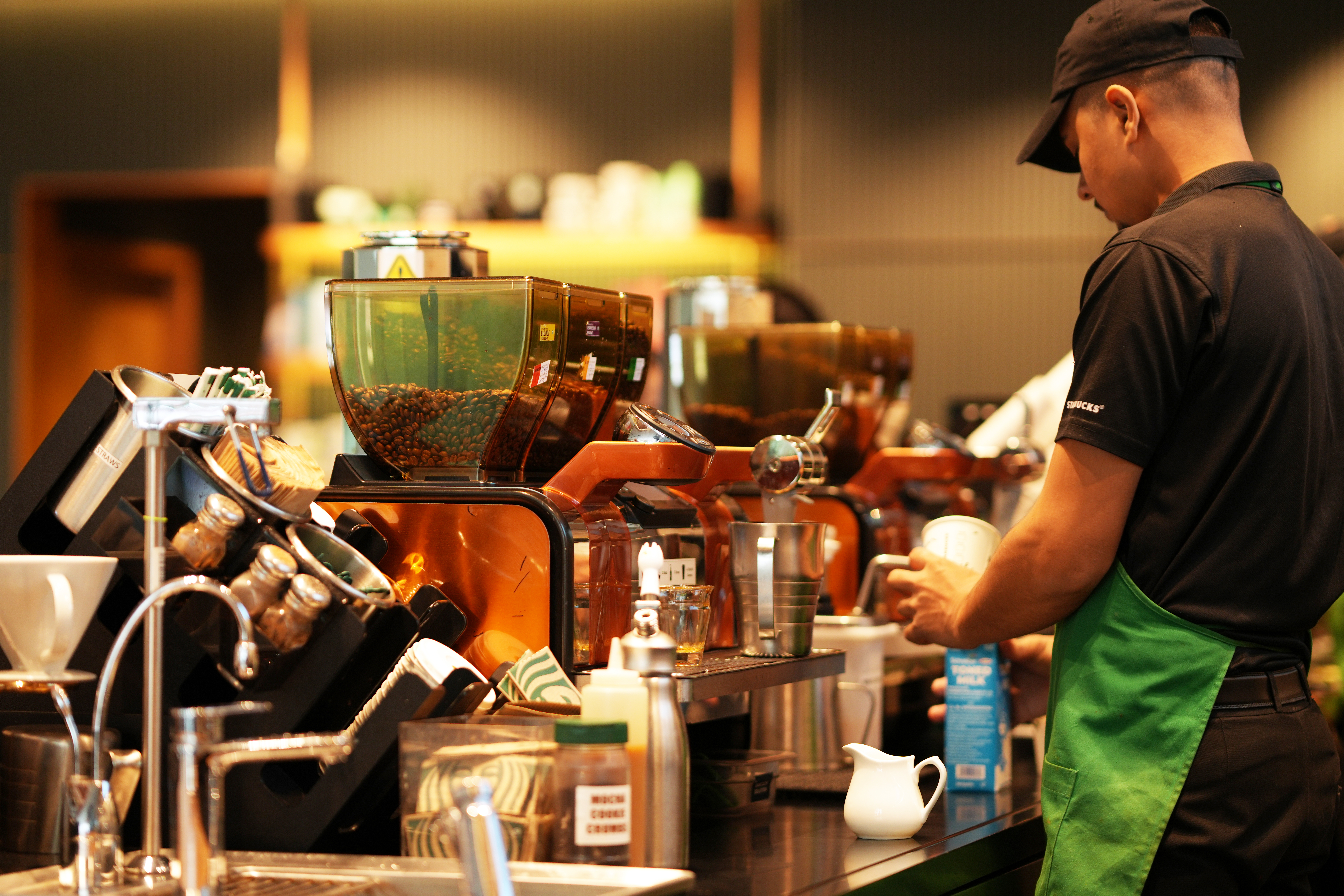 Barista frota leite em máquina de café no balcão.