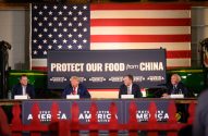 Donald Trump e 3 homens à mesa, com Trump falando. Bandeira dos EUA e banner "PROTEGER NOSSA COMIDA da CHINA" atrás.