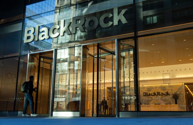 Fachada de vidro do edifício BlackRock à noite, com um homem entrando pela porta giratória.