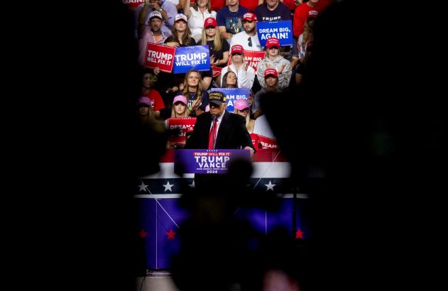 Donald Trump discursando em comício para apoiadores com cartazes "Trump Will Fix It" e "Dream Big, Again!".