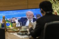 Pessoa assiste o presidente Lula em tela, com bandeira do Brasil na mesa.