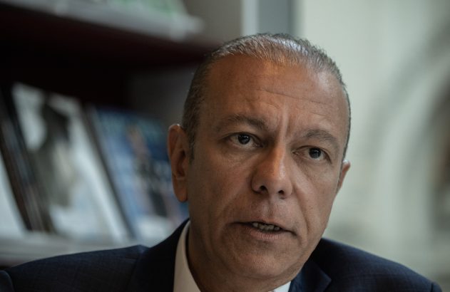 Homem de terno, com cabelo grisalho, olhando para a câmera com a boca levemente aberta, como se estivesse falando.