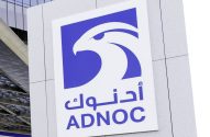 Placa com o logo azul e branco da ADNOC, que inclui um falcão, montada na parede de um edifício.