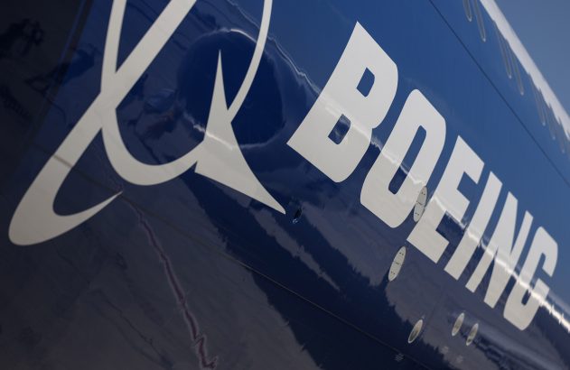 Fuselagem azul-escura de avião Boeing. Detalhe do logotipo e do nome 'BOEING' em branco, com reflexos na superfície.