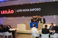 Leilão: Cinco pessoas ativam martelo simbólico no palco. Tela mostra "LEILÃO LOTE NOVA RAPOSO".