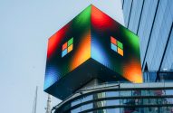 Cubo LED colorido exibindo o logo da Microsoft e cores vibrantes no topo de um prédio moderno.