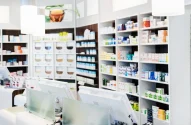 Interior moderno de uma farmácia bem iluminada, com prateleiras organizadas de medicamentos e um balcão com computadores.