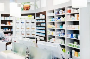 Interior moderno de uma farmácia bem iluminada, com prateleiras organizadas de medicamentos e um balcão com computadores.
