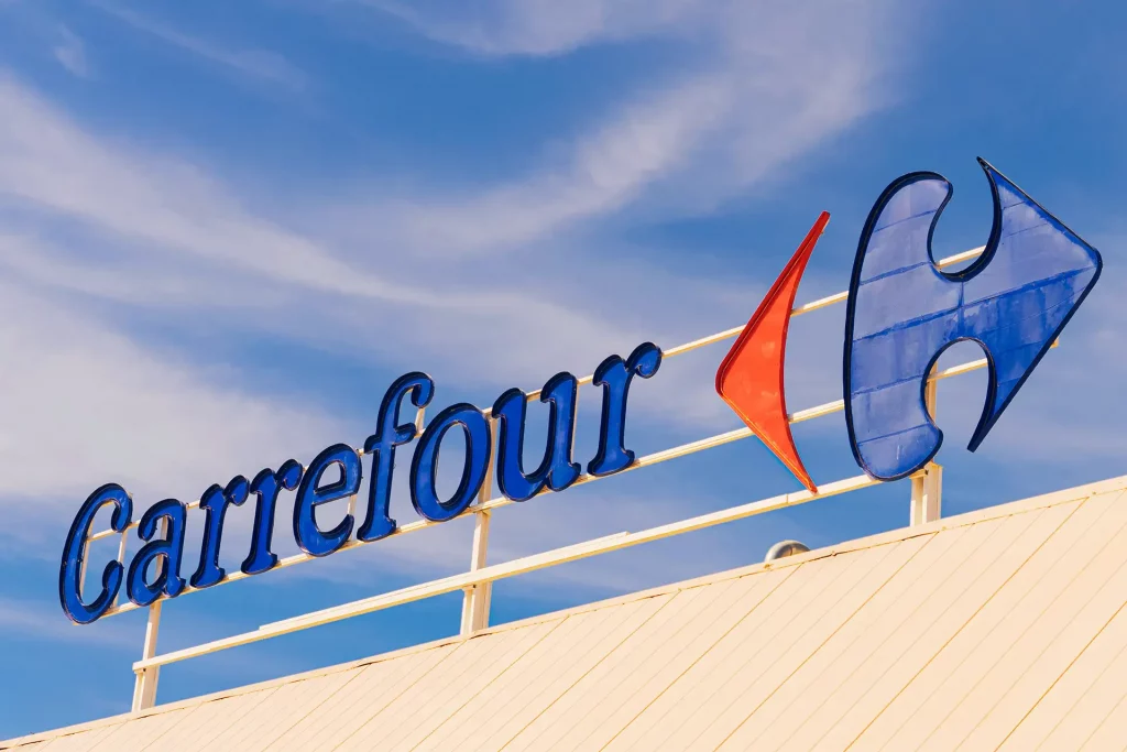 Logomarca do Carrefour destacada em um letreiro elevado contra um céu parcialmente nublado.