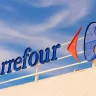 Logomarca do Carrefour destacada em um letreiro elevado contra um céu parcialmente nublado.