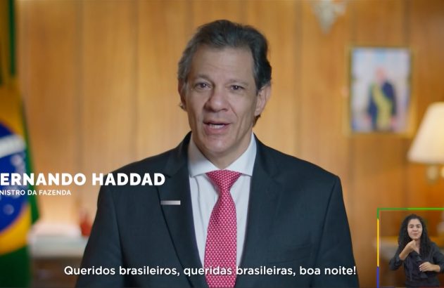 Fernando Haddad, Ministro da Fazenda, fala. À esquerda, bandeira do Brasil. À direita, intérprete de Libras.