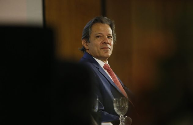 Homem de terno azul e gravata vermelha, cabelos grisalhos, olhando para o lado com leve sorriso.