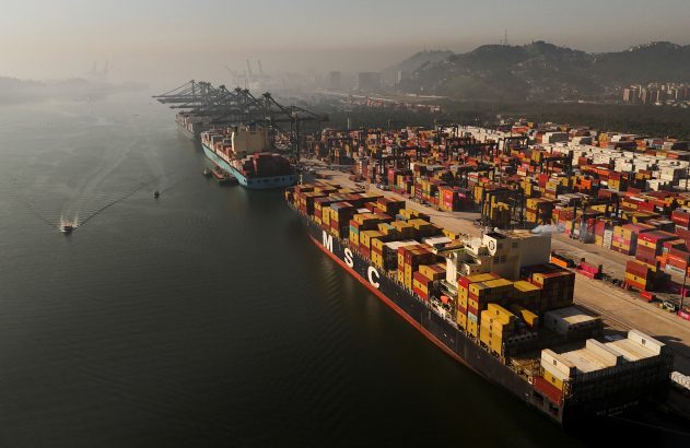 Porto de contêineres movimentado com navios, guindastes e milhares de contêineres empilhados.