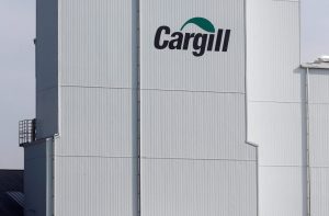 Prédio da Cargill, branco com logo verde, e dois caminhões próximos a uma cerca e gramado em dia claro.