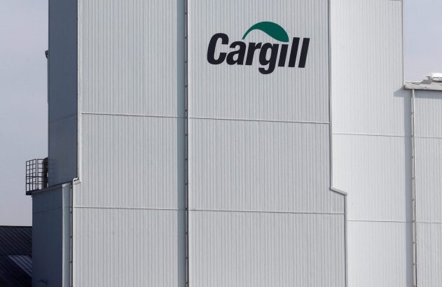 Prédio da Cargill, branco com logo verde, e dois caminhões próximos a uma cerca e gramado em dia claro.