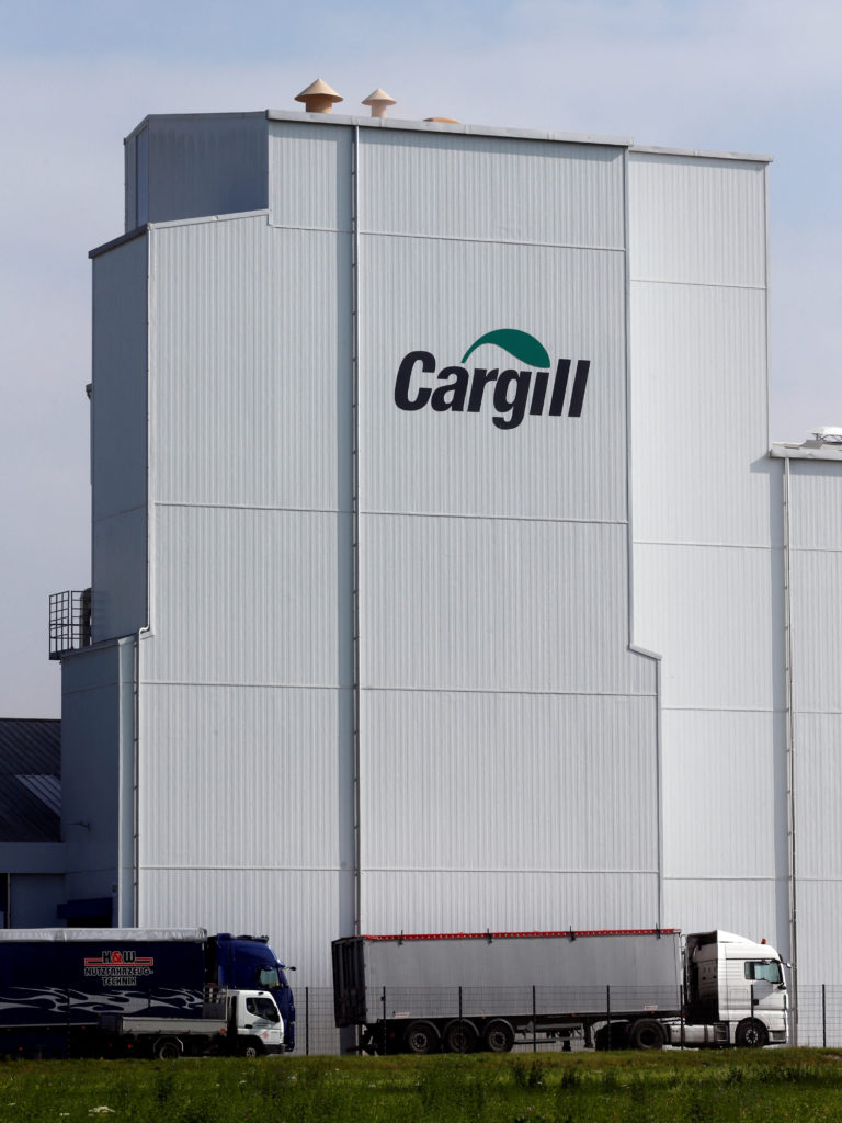 Prédio da Cargill, branco com logo verde, e dois caminhões próximos a uma cerca e gramado em dia claro.