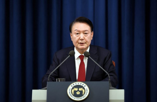 Presidente Yoon Suk Yeol, de terno e gravata vermelha, discursa em pódio com microfones.