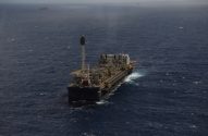 Plataforma de petróleo flutuante (FPSO) no mar agitado. Outras embarcações visíveis ao longe.