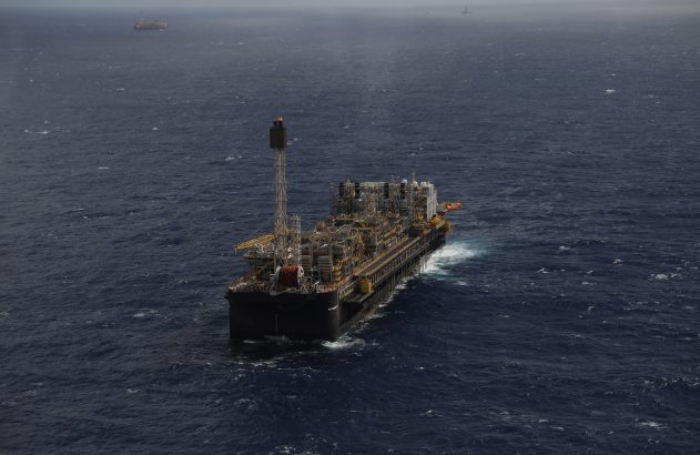 Plataforma de petróleo flutuante (FPSO) no mar agitado. Outras embarcações visíveis ao longe.