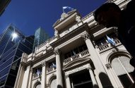 Banco Central da Argentina, prédio clássico com bandeiras e relógio, contrastando com edifícios modernos. Pessoa à direita.