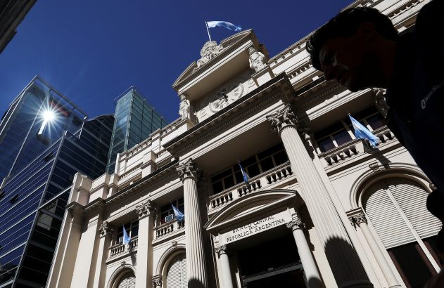 Banco Central da Argentina, prédio clássico com bandeiras e relógio, contrastando com edifícios modernos. Pessoa à direita.
