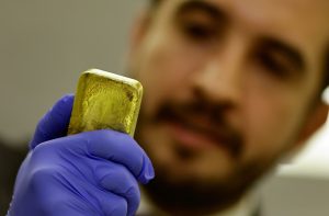 Homem de luvas azuis examinando uma barra de ouro.