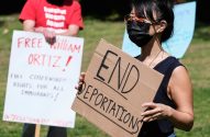 Mulher de máscara em protesto segura cartaz "END DEPORTATIONS". Ao lado, outra pessoa exibe cartaz "FREE WILLIAM ORTIZ".