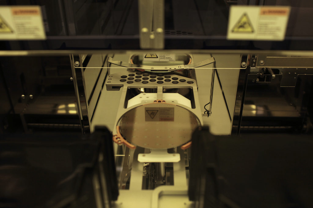 Wafer de silício sendo processado por máquina automatizada de fabricação de semicondutores.