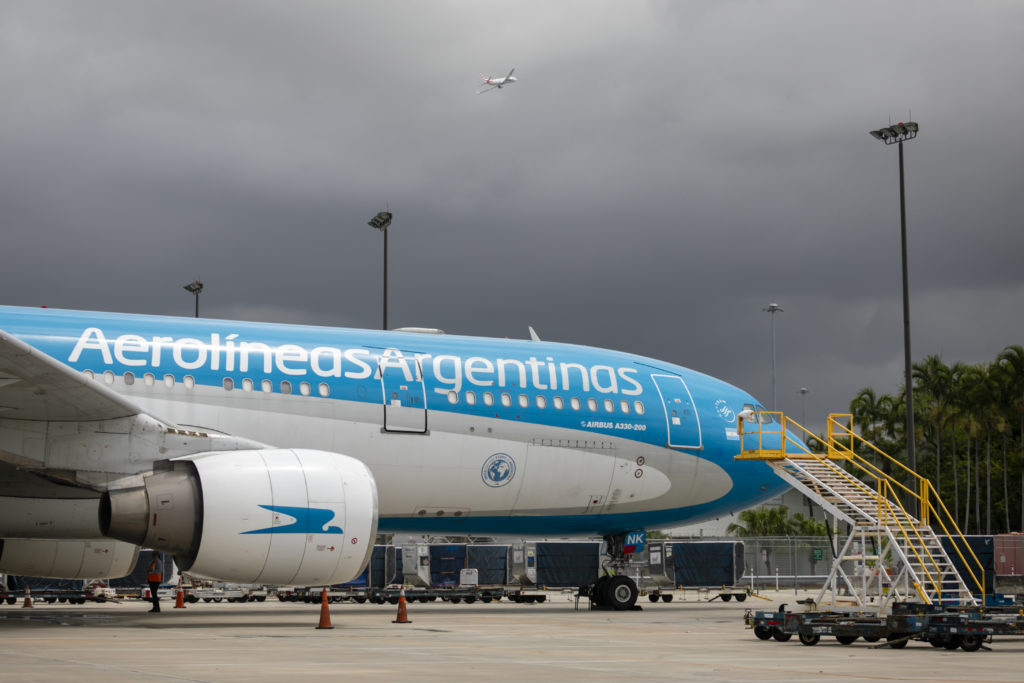 Avião Aerolíneas Argentinas Airbus A330-200 no pátio do aeroporto sob céu nublado. Outro avião menor no céu.