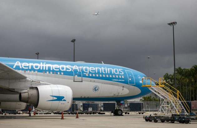 Avião Aerolíneas Argentinas Airbus A330-200 no pátio do aeroporto sob céu nublado. Outro avião menor no céu.