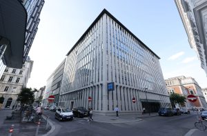 Edifício moderno da OPEP, com fachada vertical, em um cruzamento de rua movimentado com pessoas e veículos em Viena.