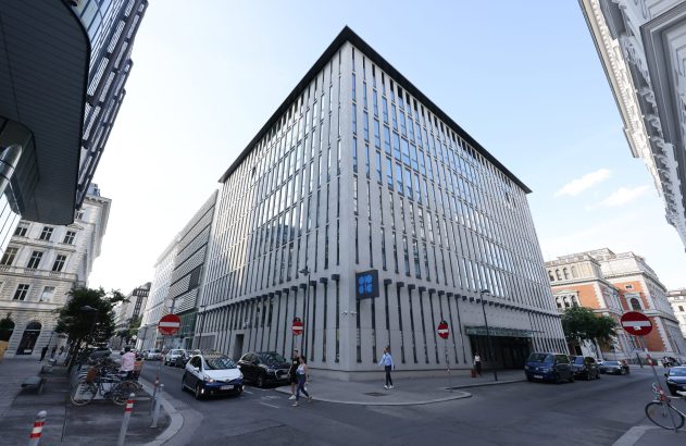 Edifício moderno da OPEP, com fachada vertical, em um cruzamento de rua movimentado com pessoas e veículos em Viena.