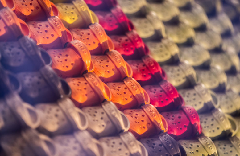 Fileiras de sapatos Crocs coloridos, incluindo laranja, vermelho, amarelo e cinza.