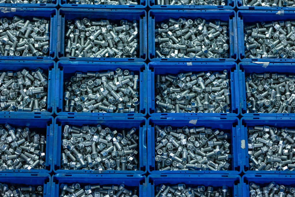 Caixas plásticas azuis empilhadas, repletas de parafusos metálicos prateados.